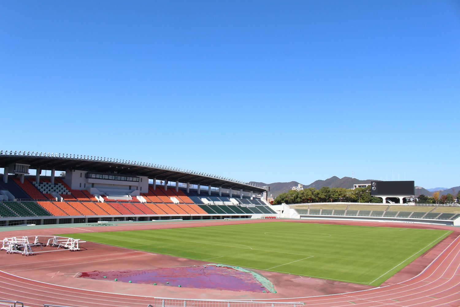 青空の下の長良川競技場の全景。芝生フィールドと陸上トラック、観客席が見える。