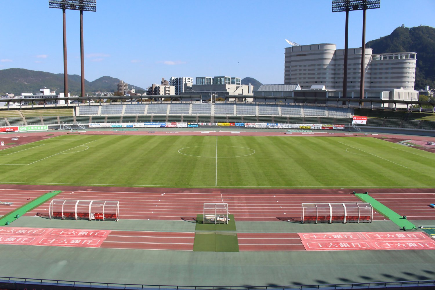 青空の下の長良川競技場。芝生のフィールドと陸上トラック、ベンチ、観客席が正面に広がっている。